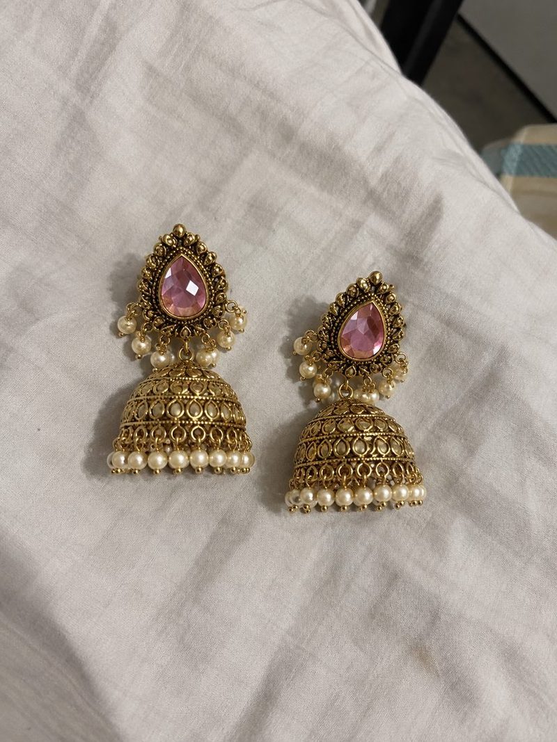 Phone photo of a pair of gold jhumka earrings with pink stones on a white sheet